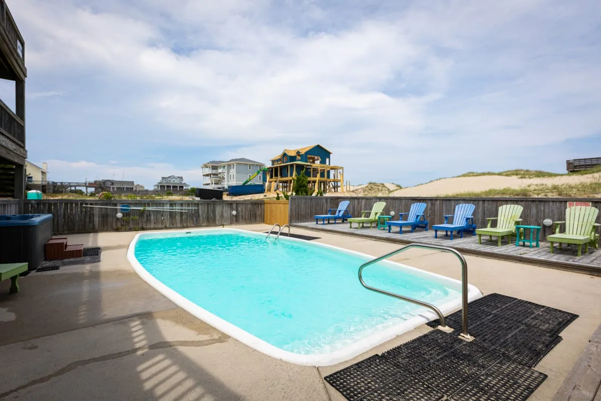 An outdoor swimming pool is surrounded by lounge chairs and a wooden fence.
