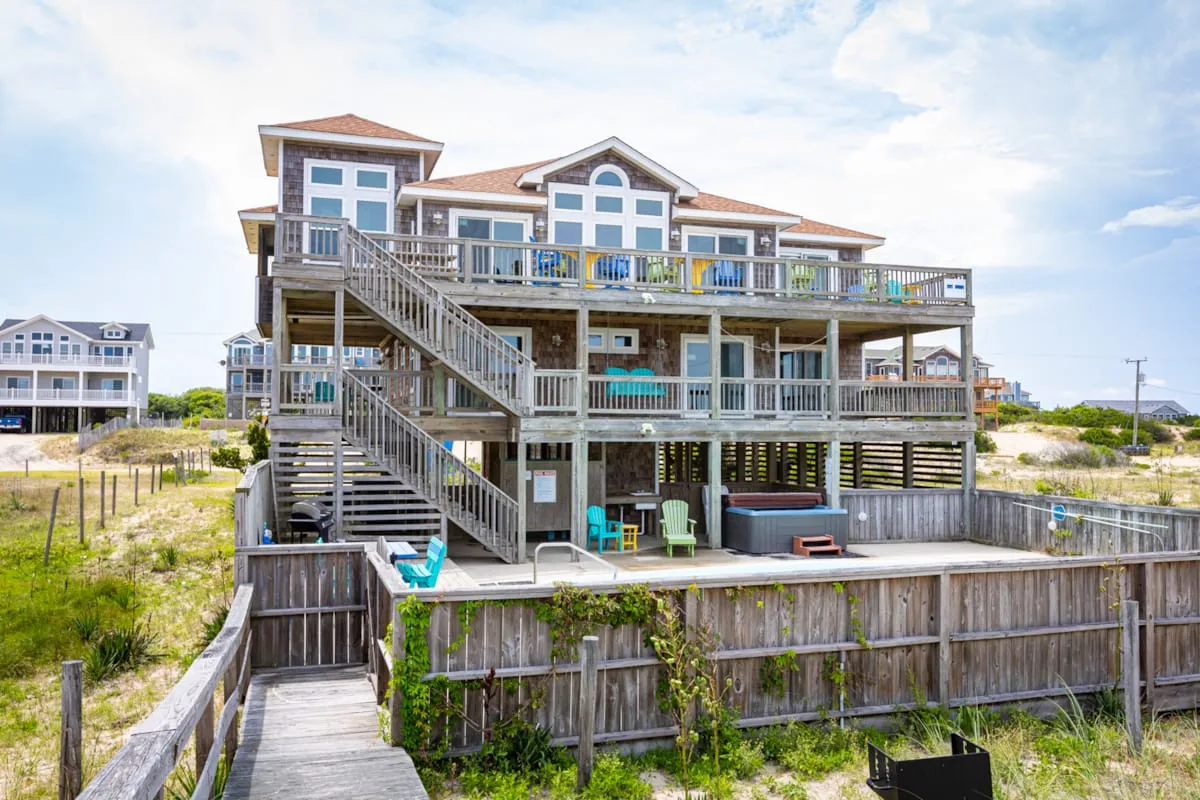 A large elevated beach house with wooden decks and exterior stairways.