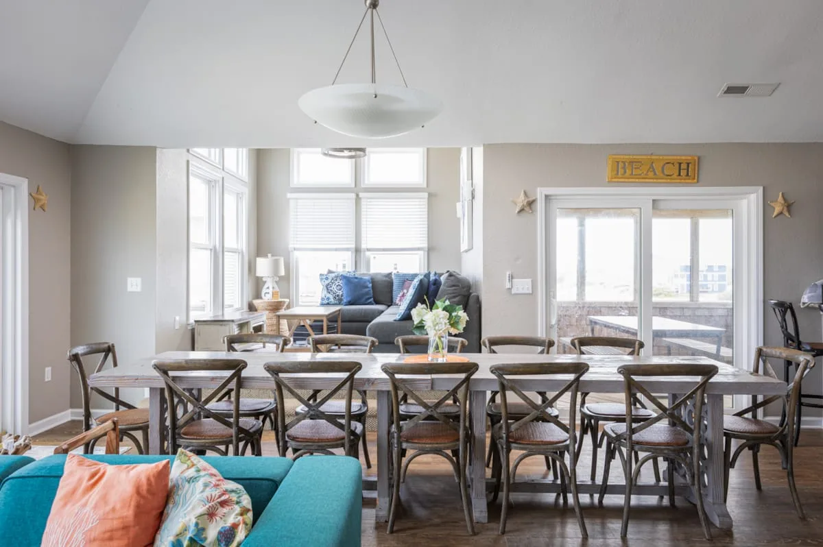 A bright dining area with a long table and seating beside a living space.
