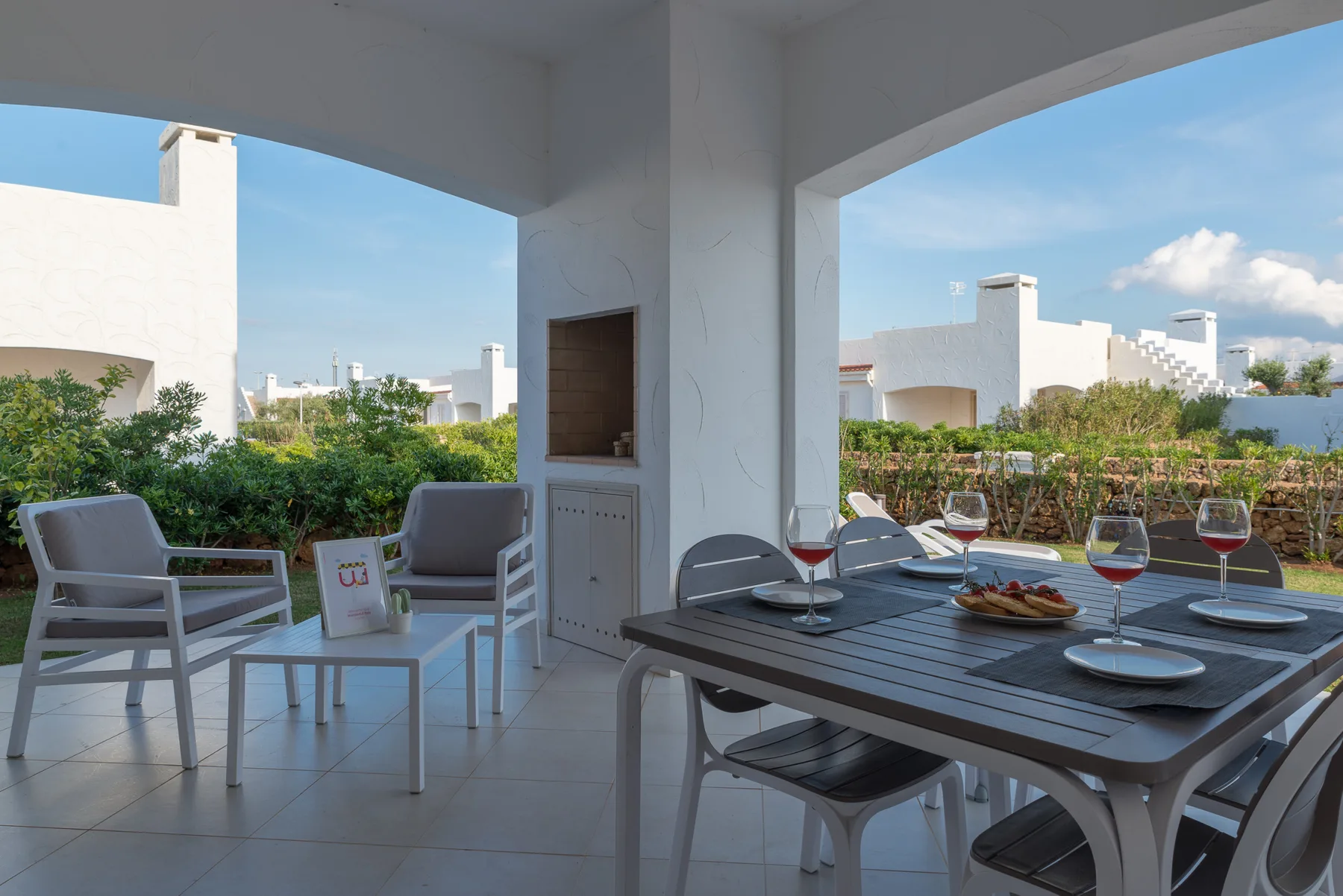 A covered outdoor dining area with a table and seating overlooking a garden.