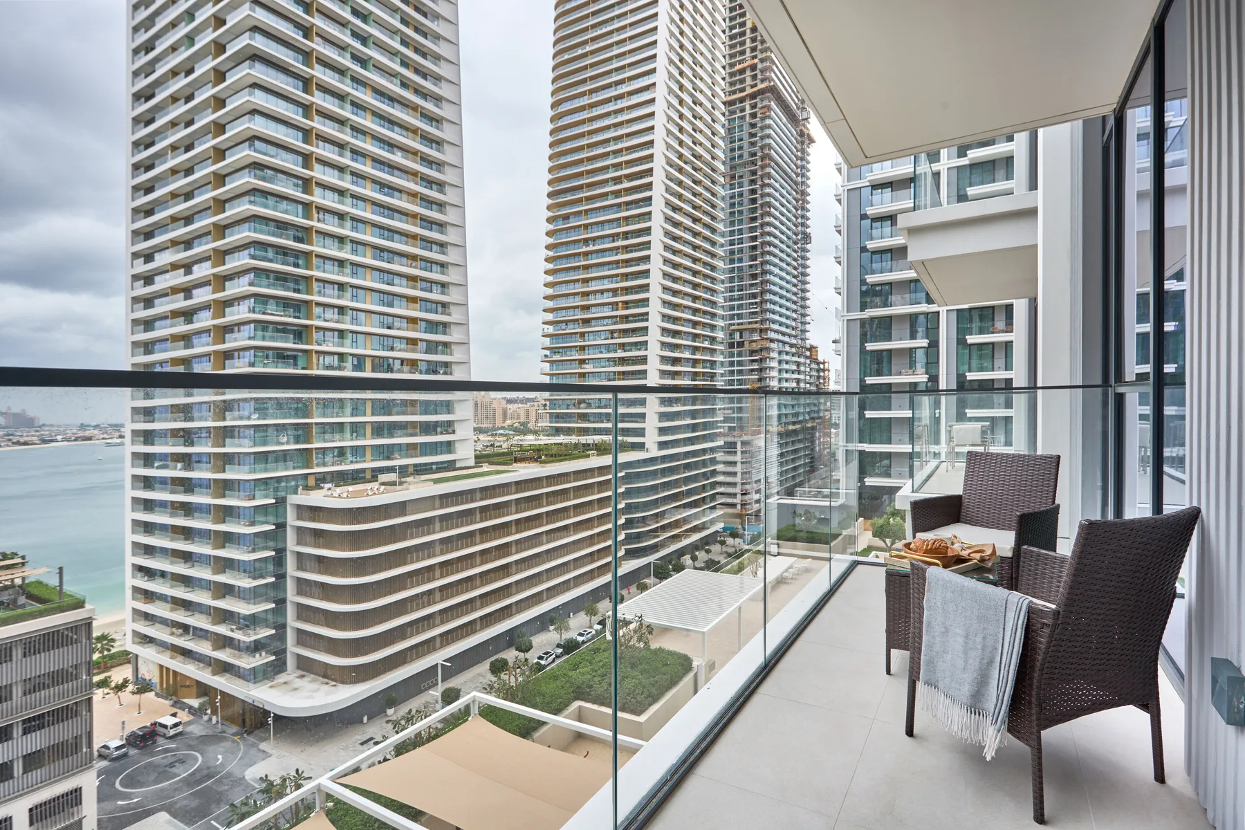 A balcony with seating overlooks nearby high-rise buildings and the waterfront.