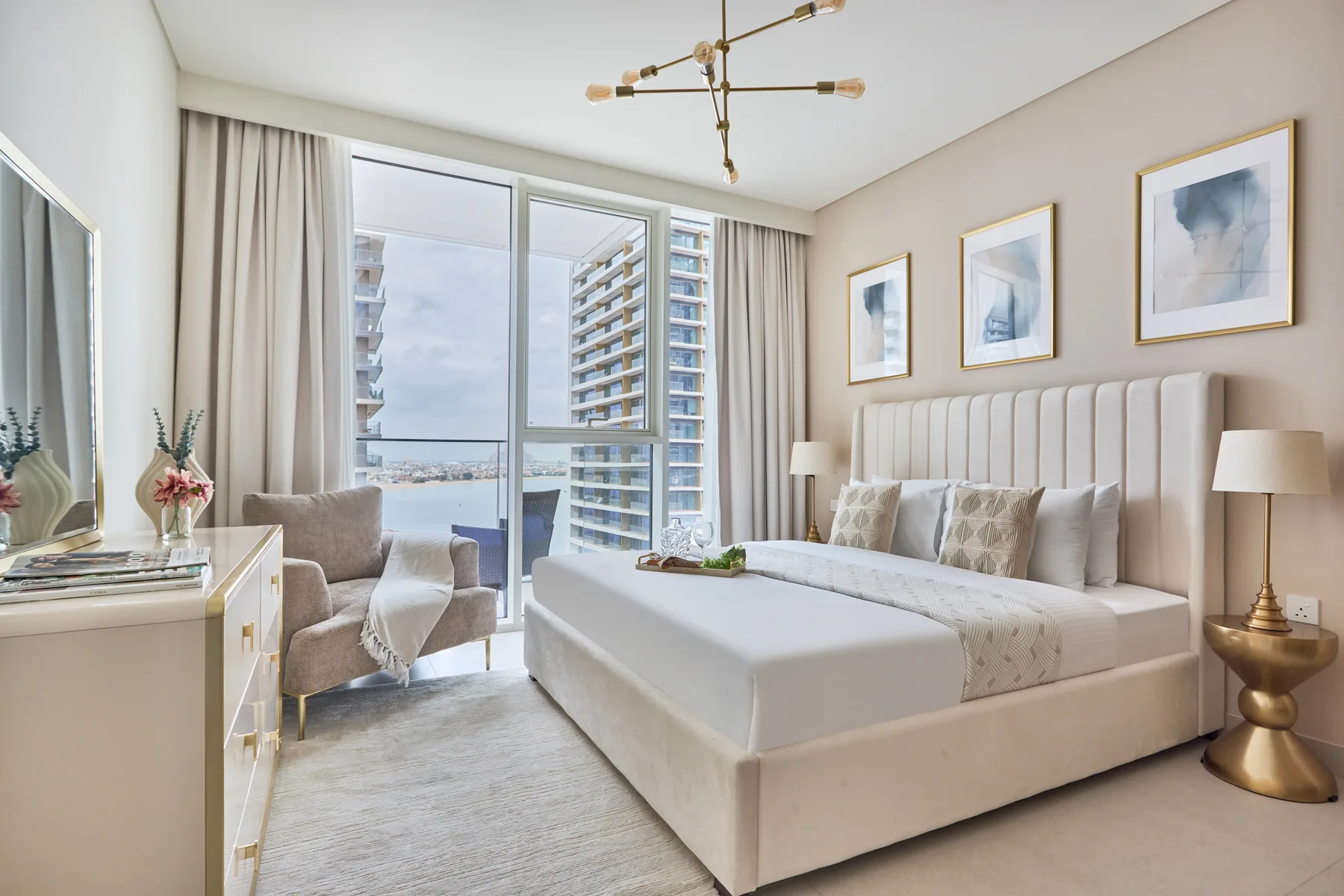 A bright bedroom with a large bed beside windows overlooking nearby buildings.