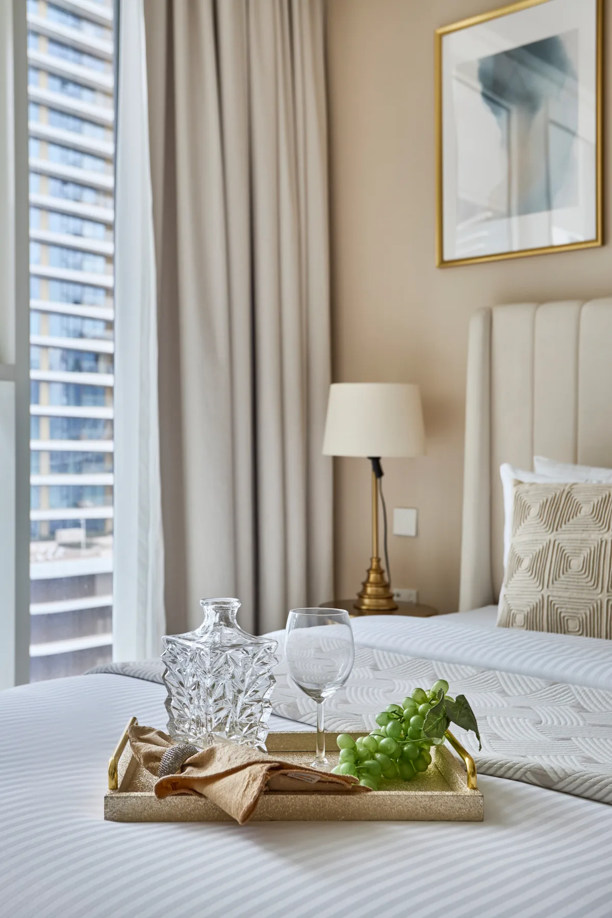 A bedroom with a neatly made bed, bedside lamp, and a tray of grapes.