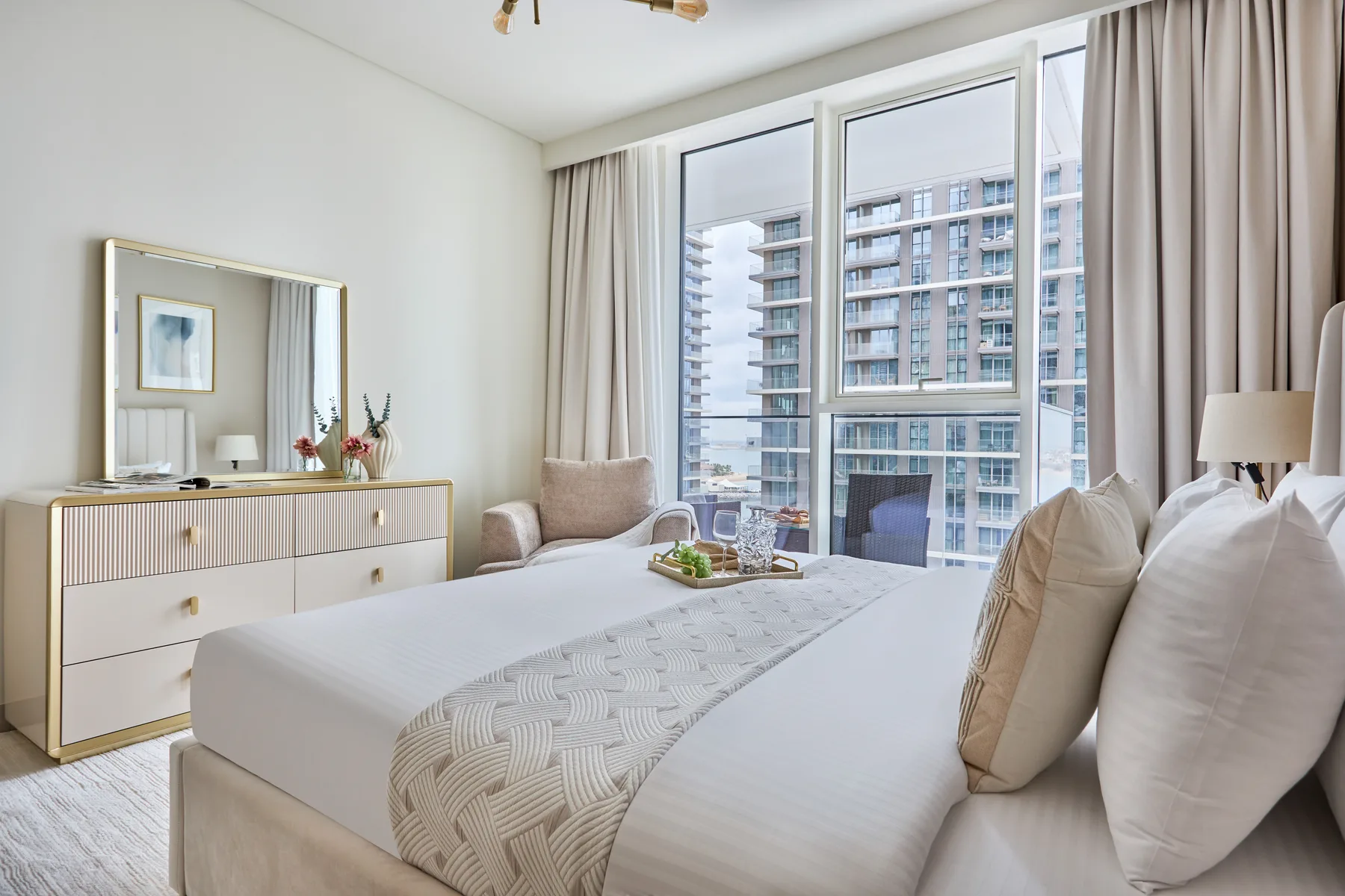 A bright bedroom with a neatly made bed beside large windows.