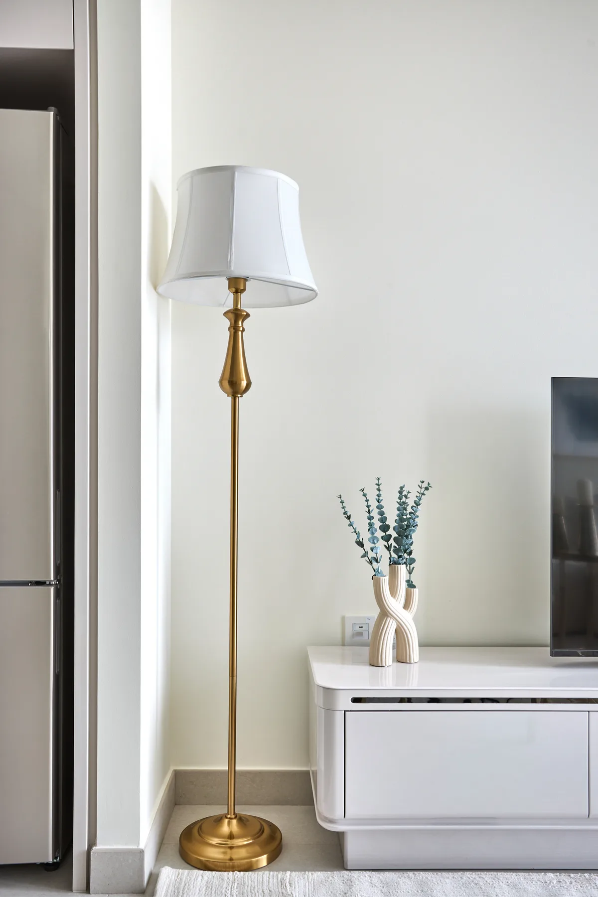 A bright living room corner with a brass floor lamp and a white media console.