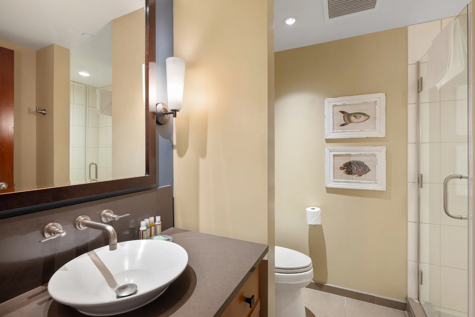 Un tocador de baño con lavabo y espejo está junto a una ducha y un inodoro.