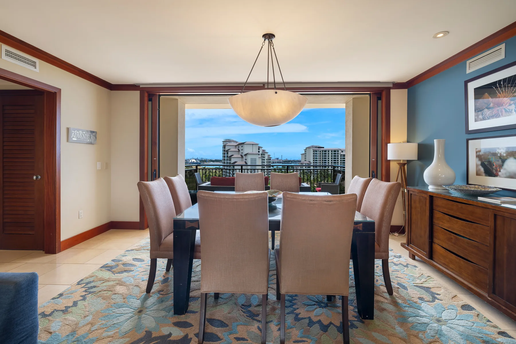 A dining area with a table and seating opens onto a balcony with a city view.