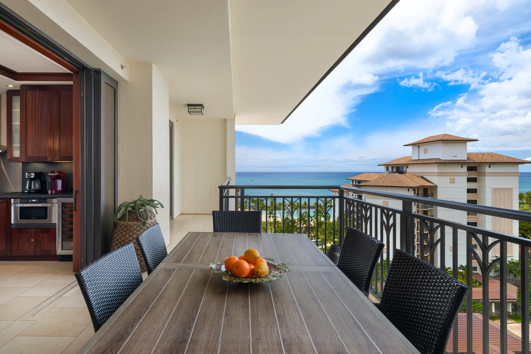 A balcony dining area overlooks the ocean, with a table and chairs beside the railing.