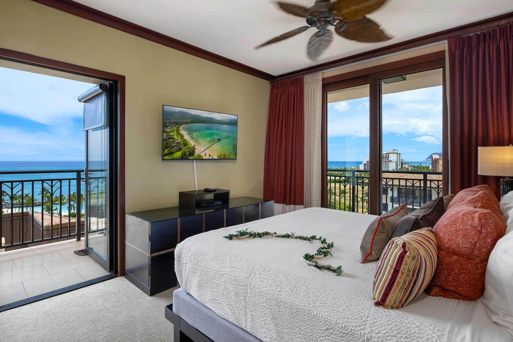Un dormitorio con cama, televisor y puertas al balcón con vistas al mar.