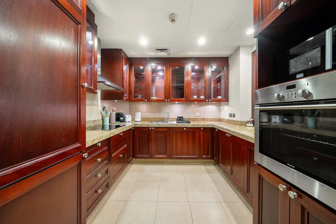 Una cocina con armarios de madera oscura, encimeras de azulejos y electrodomésticos integrados.