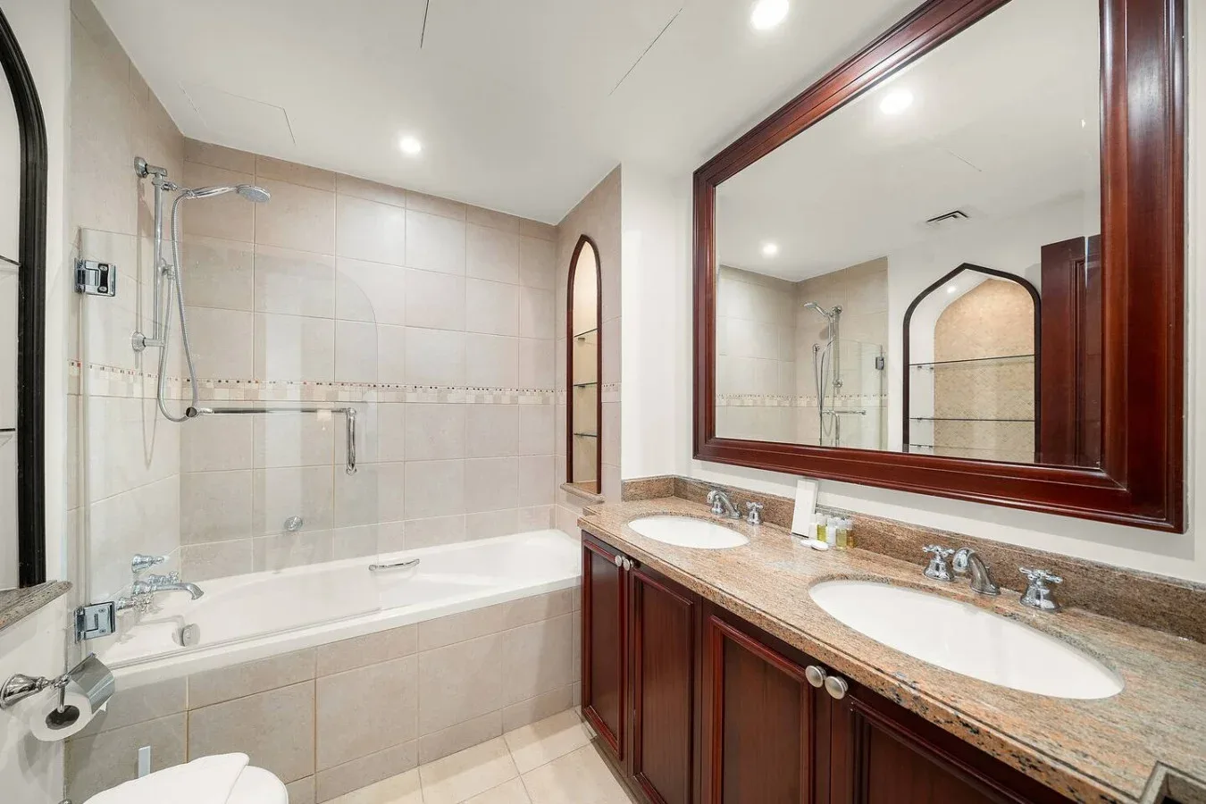Baño con bañera, ducha y tocador con dos lavabos.