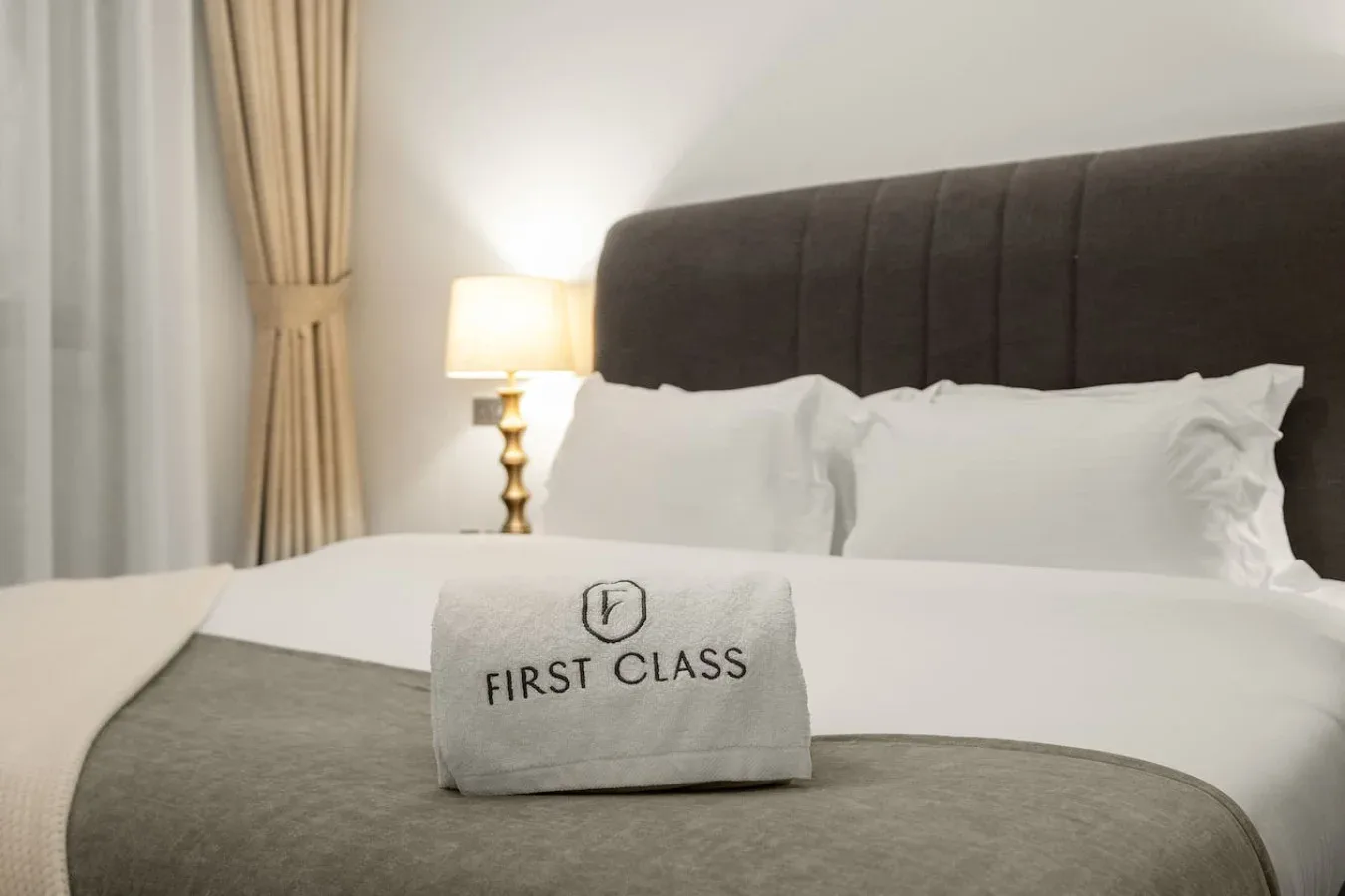 Un dormitorio bien arreglado con ropa de cama blanca y un cabecero oscuro tapizado.
