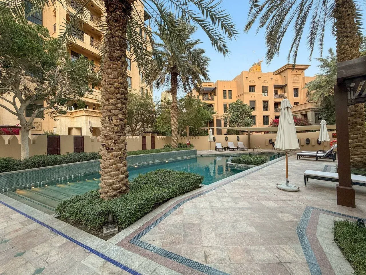 Una piscina está rodeada de palmeras, asientos y edificios de apartamentos.