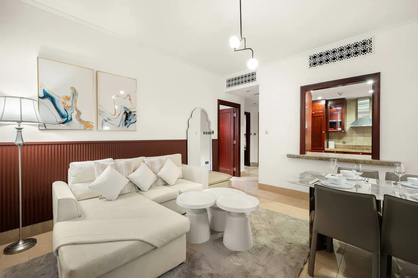 Una luminosa sala de estar y comedor cuenta con asientos claros y una pared decorativa de madera oscura.