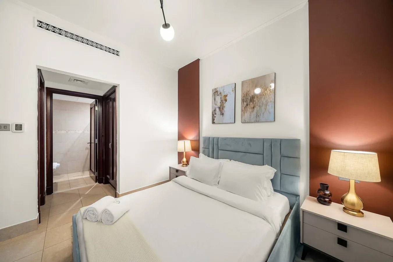 Un dormitorio con una cama, mesitas de noche y cuadros sobre el cabecero.