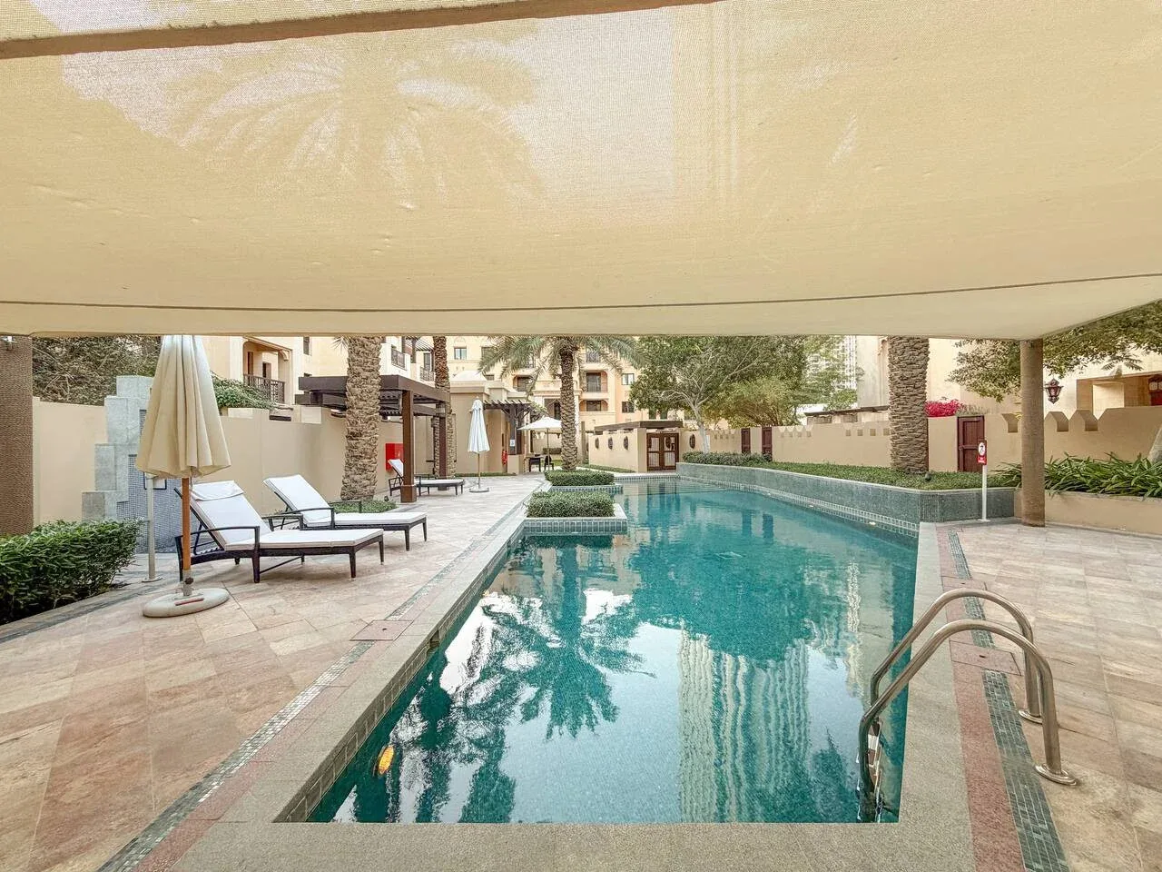 Una piscina en un patio está rodeada de caminos pavimentados y asientos.