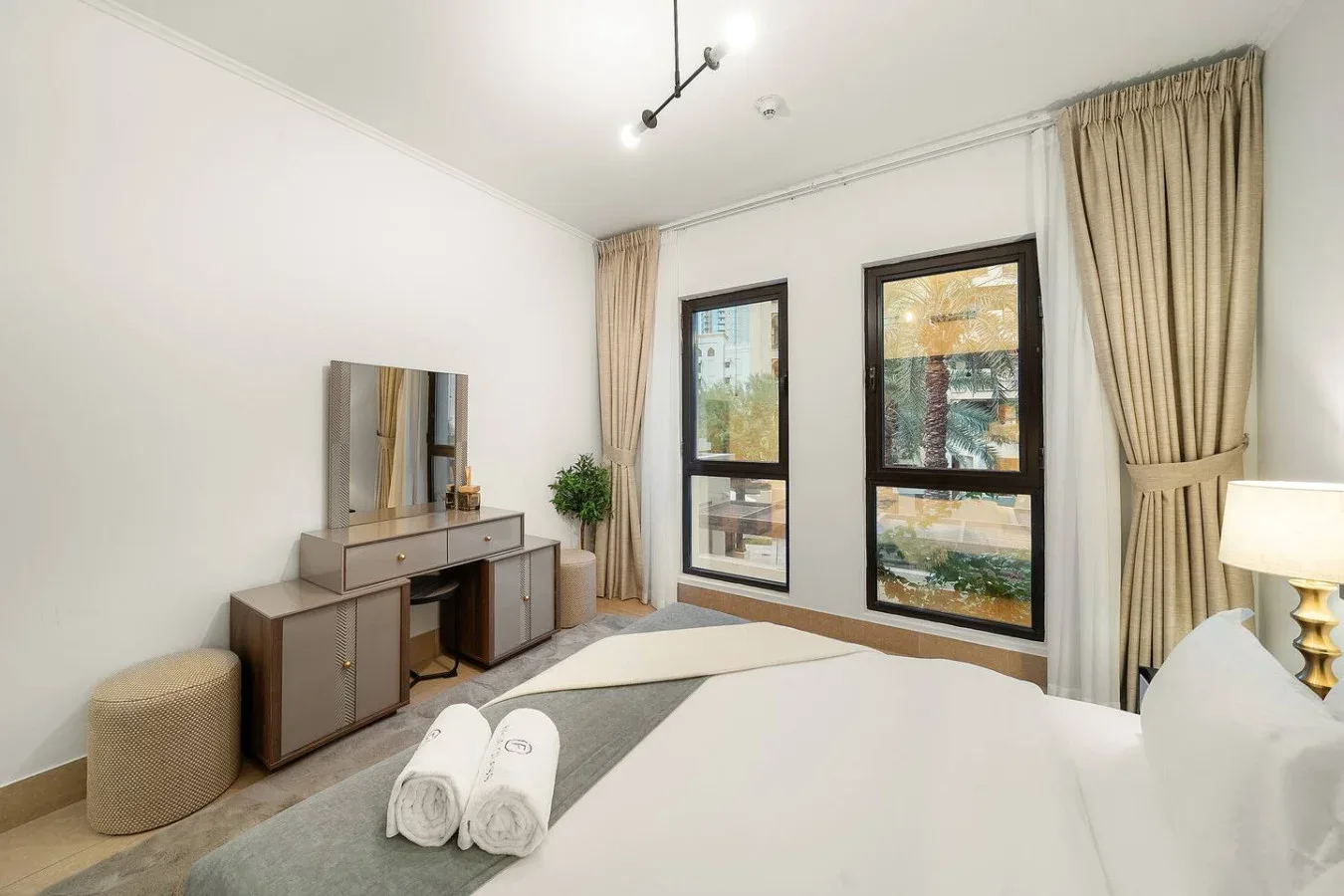 Dormitorio con cama, tocador y ventanas grandes.