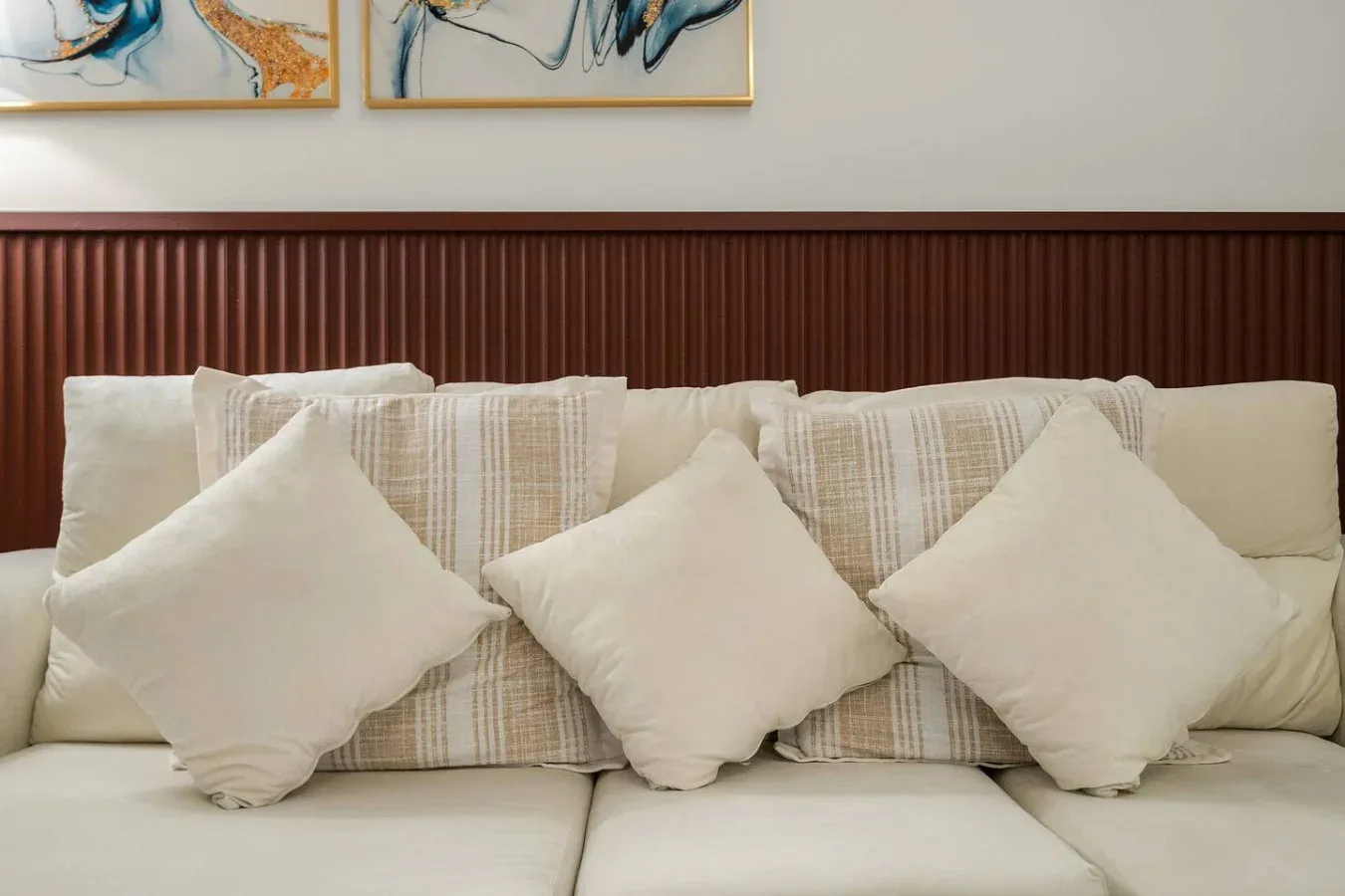 Una zona de estar con cojines claros junto a una pared revestida de madera.