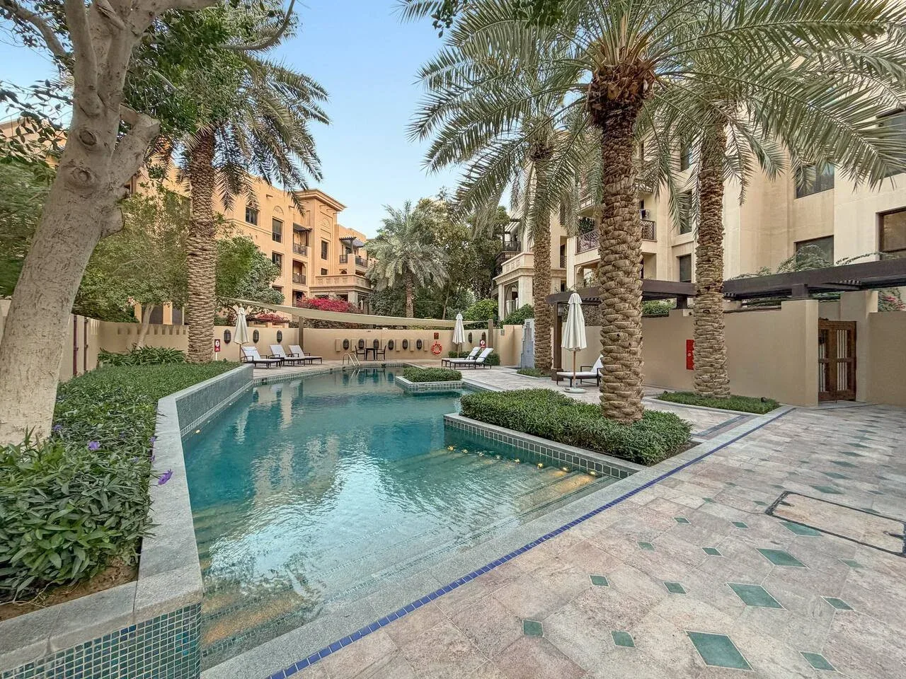Una piscina en un patio está rodeada de palmeras y edificios de apartamentos.