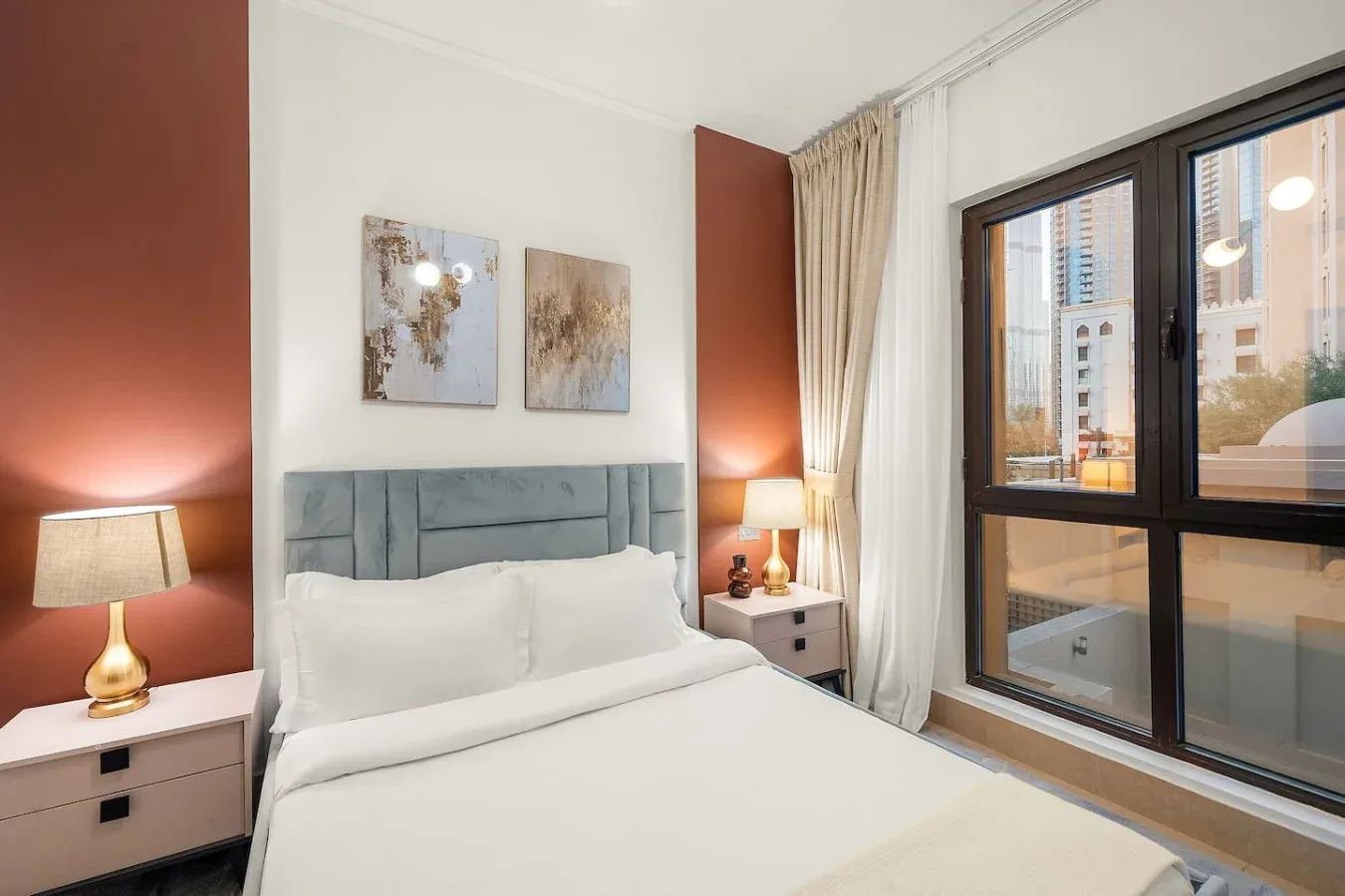 Un dormitorio con una cama bien tendida, mesitas de noche y ventanas grandes.