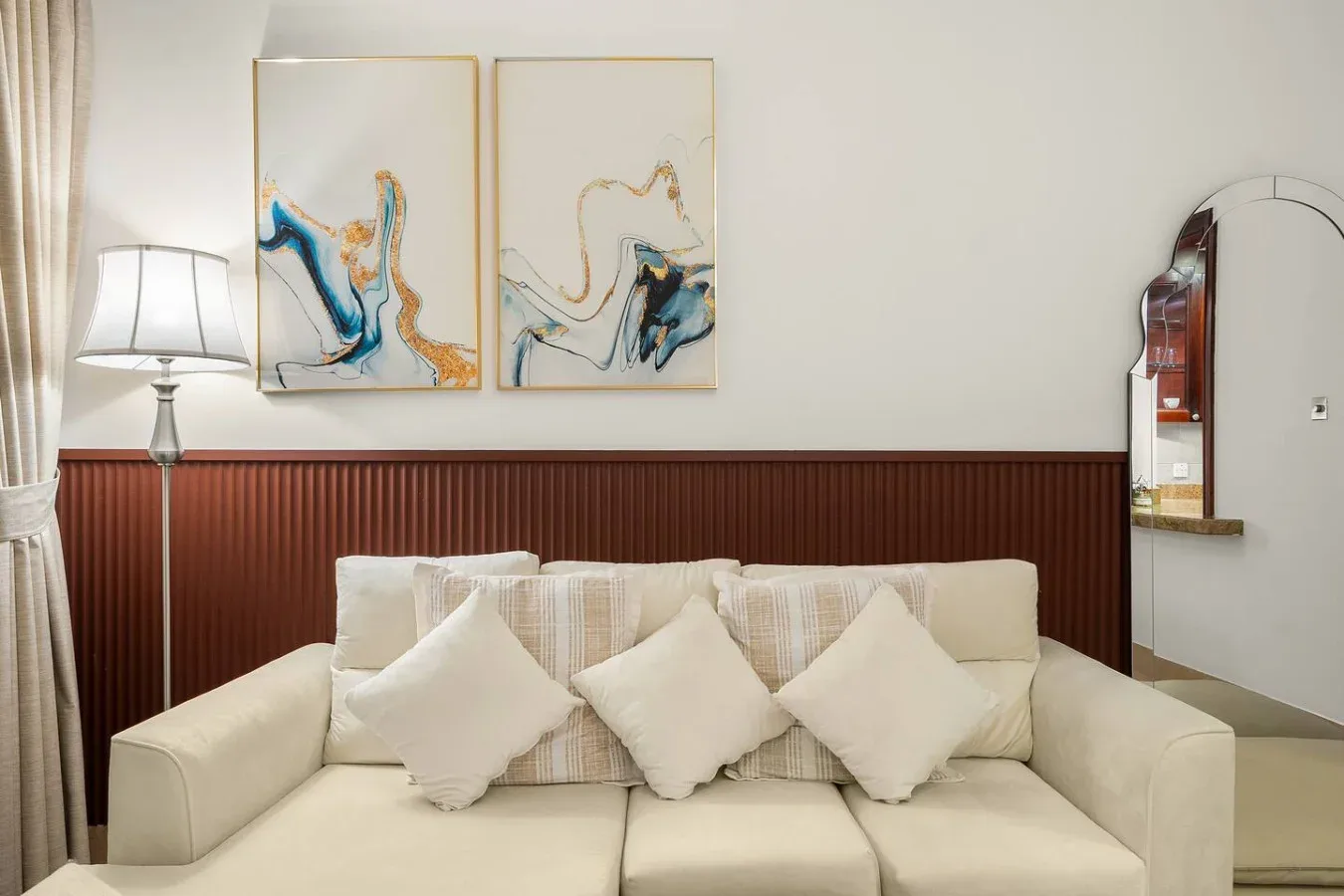 Sala de estar con asientos claros, cojines decorativos y cuadros abstractos.