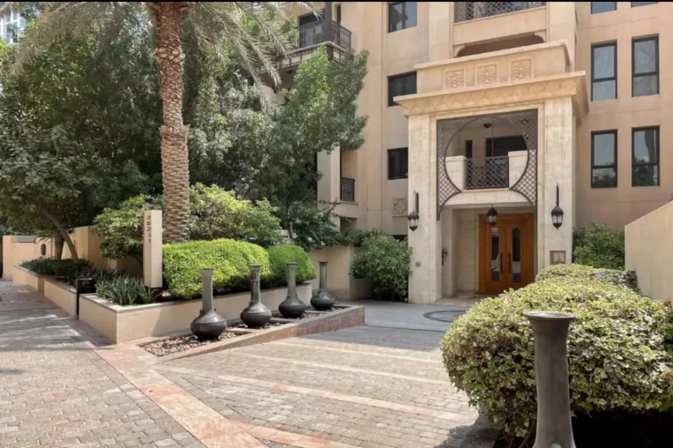 Un patio ajardinado con un camino pavimentado conduce a la entrada ornamentada de un edificio.