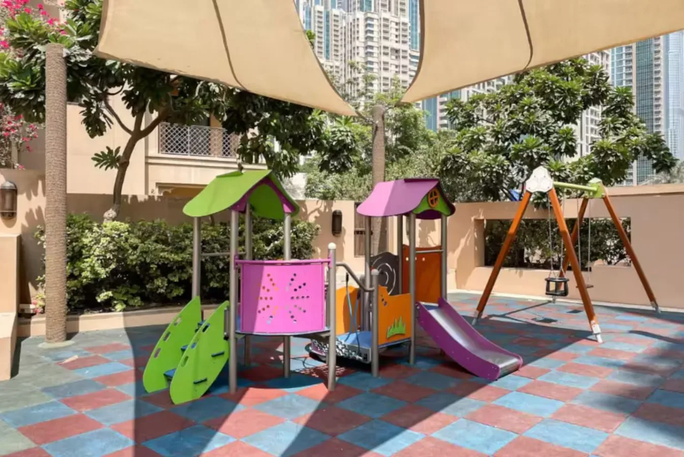 Un parque infantil al aire libre con juegos coloridos y columpios bajo toldos.