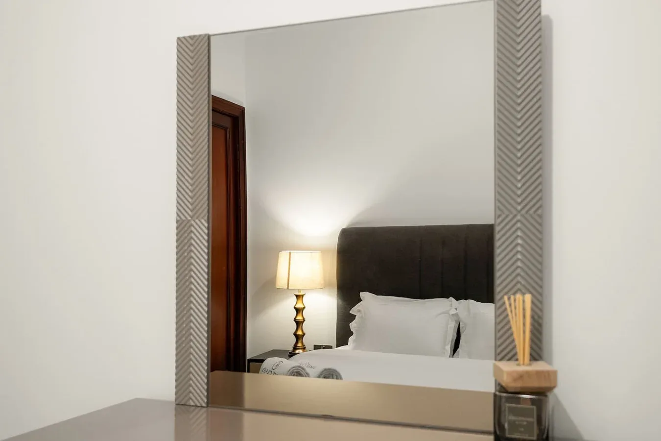 Un dormitorio con una cama, una lámpara de noche y un gran espejo de pared.