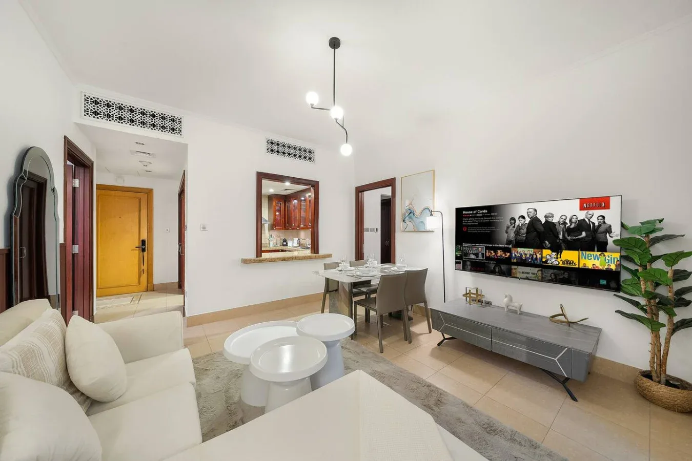 Una sala de estar luminosa con zona de descanso, mesa de comedor y televisor en la pared.