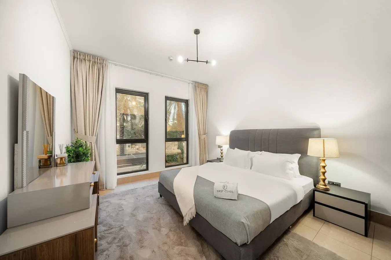 Un dormitorio luminoso con una cama bien tendida y ventanas altas.