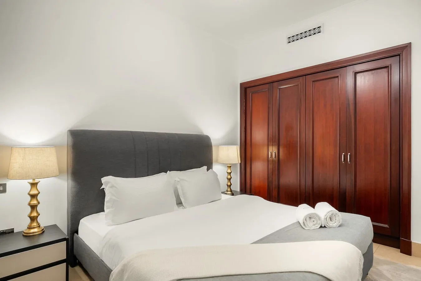 Un dormitorio con una cama bien hecha y un armario de madera oscura.