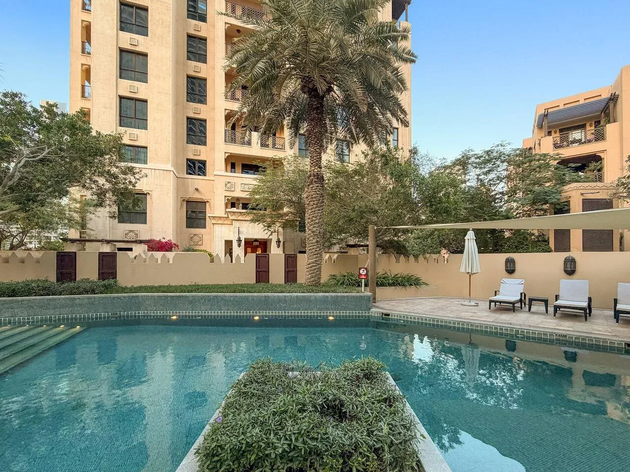 Una piscina al aire libre está junto a jardines y edificios de apartamentos.