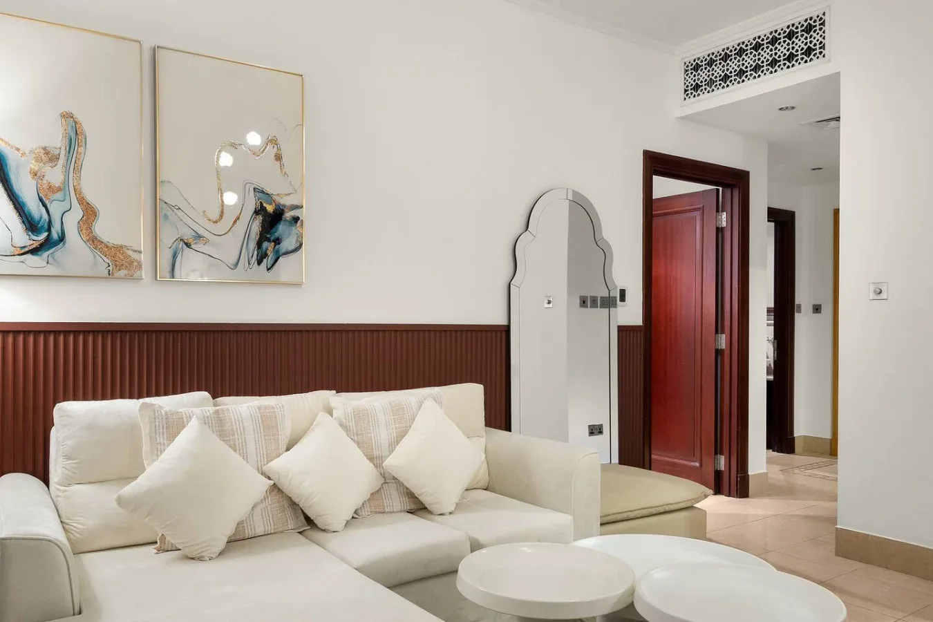 Sala de estar con asientos claros, cojines decorativos y cuadros en la pared.