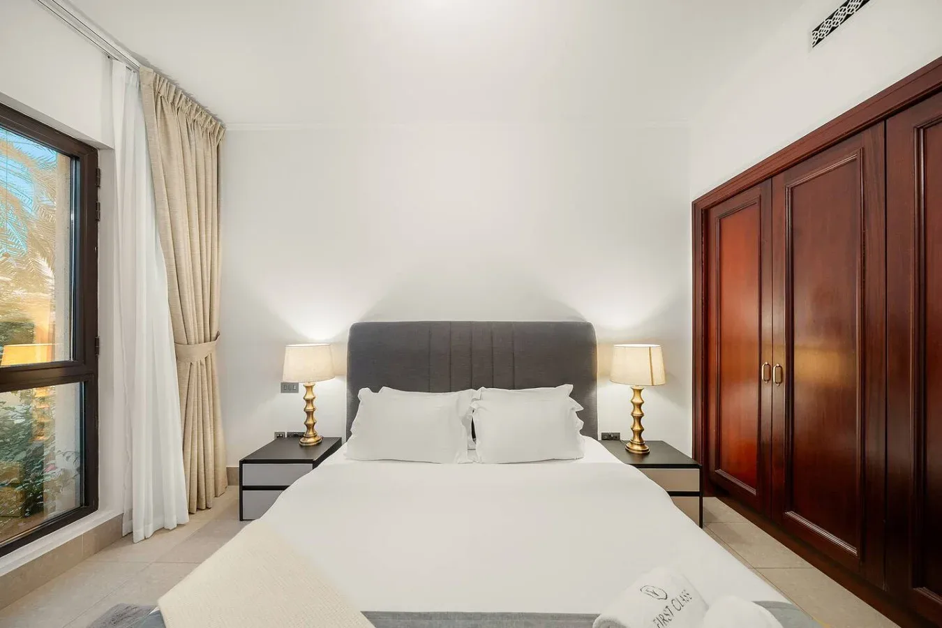 Un dormitorio con una cama hecha, mesas de noche y un armario.