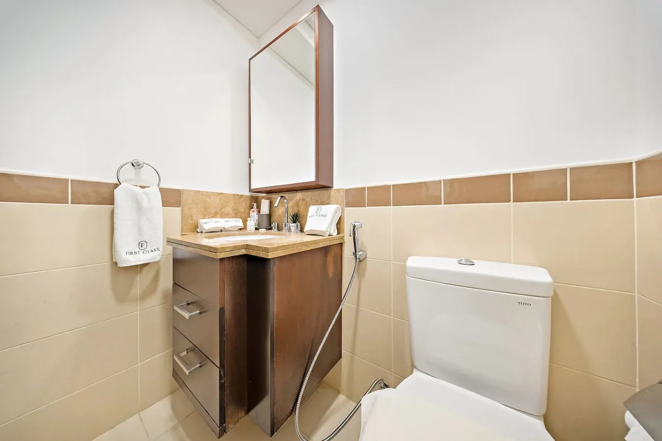 Un baño con azulejos, tocador de madera, espejo e inodoro.