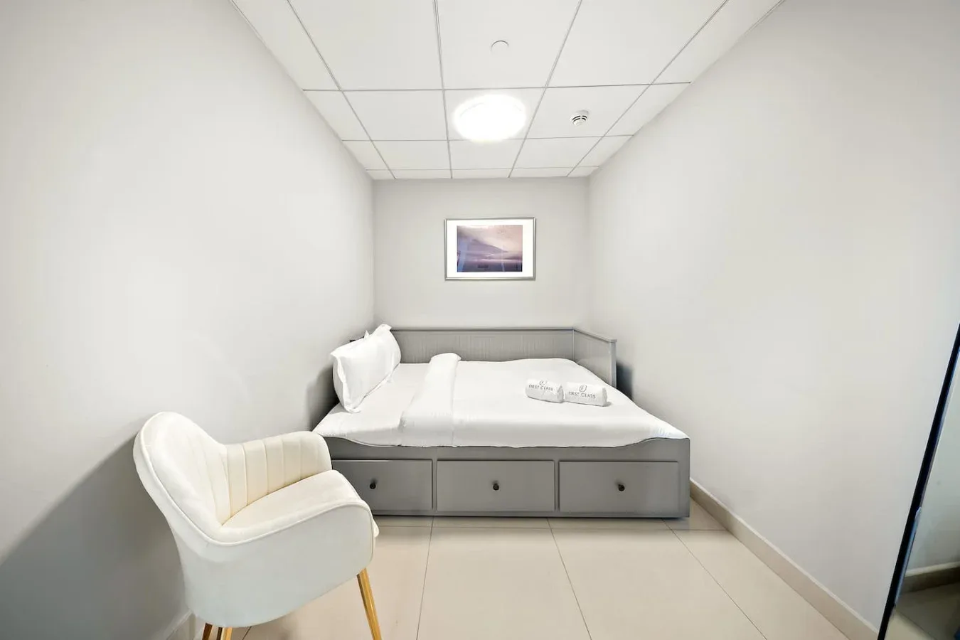 Un dormitorio compacto con una cama individual y una silla tapizada.