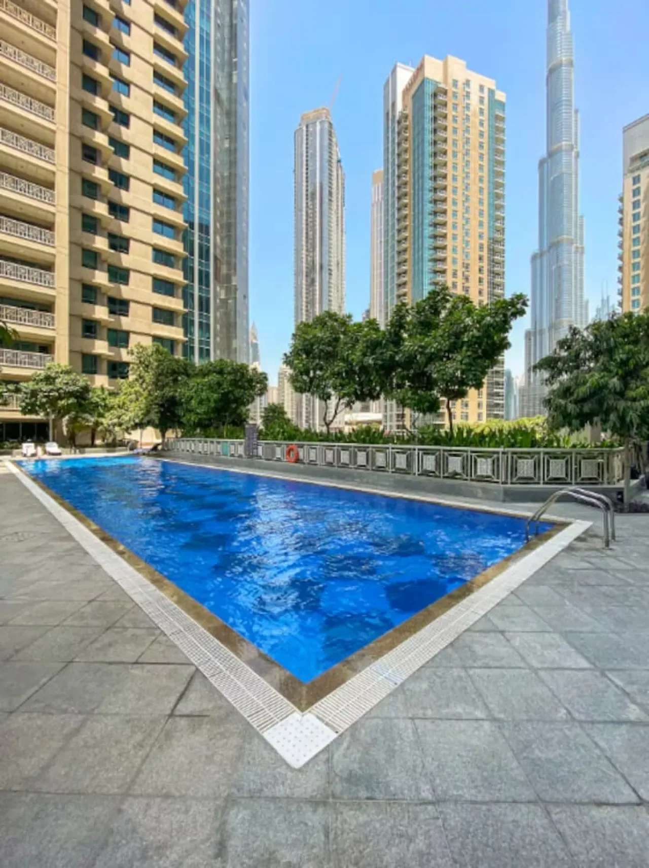 Una piscina al aire libre está rodeada de edificios altos y árboles.
