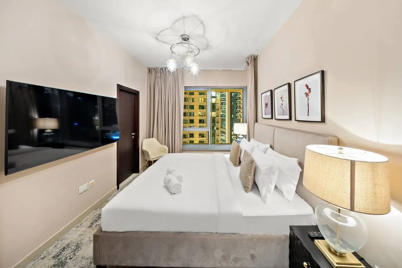 Dormitorio con una cama grande, televisor montado en la pared y una ventana con cortinas.