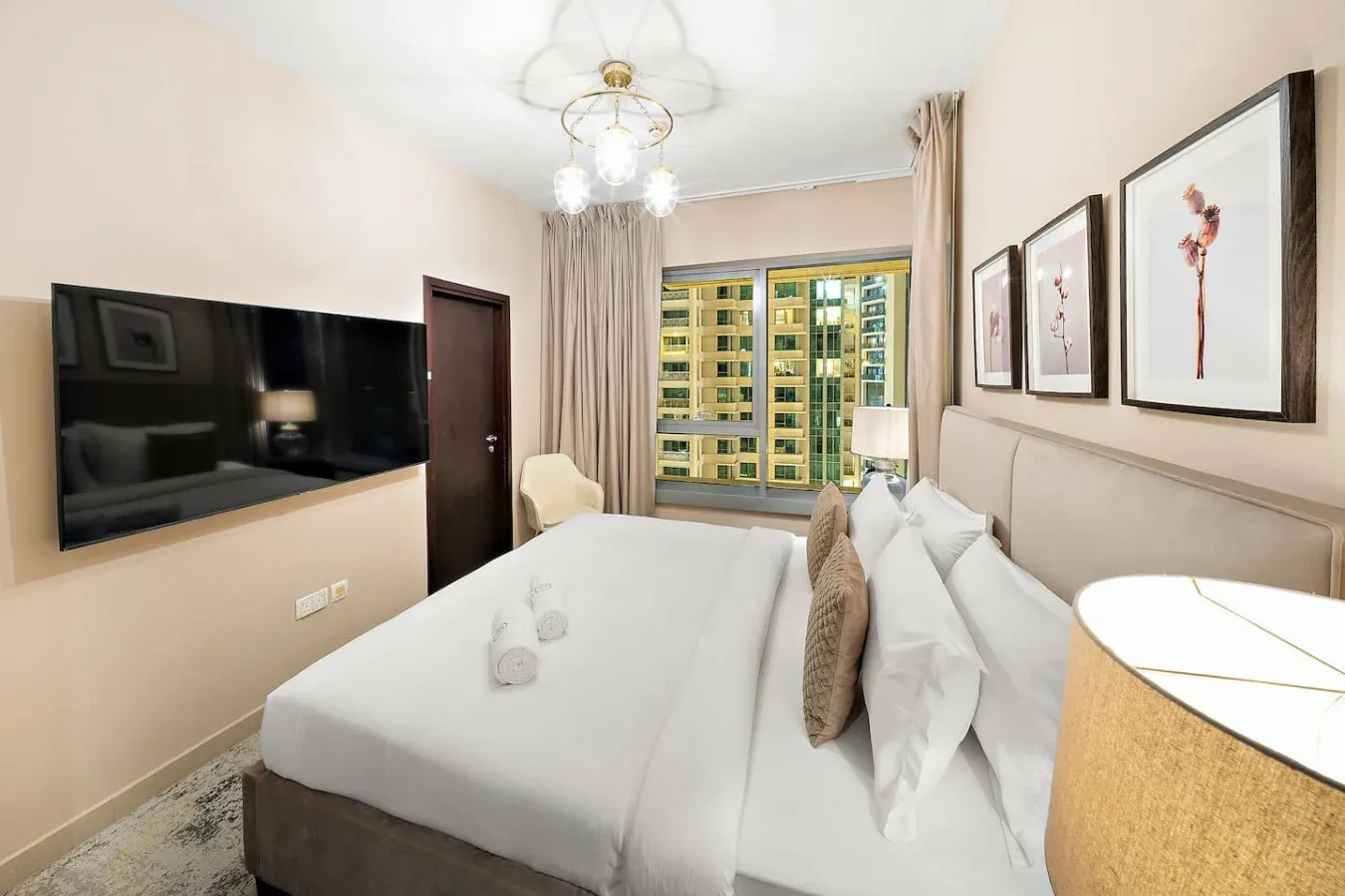 Un dormitorio con una cama bien tendida, un televisor en la pared y ventanas amplias.