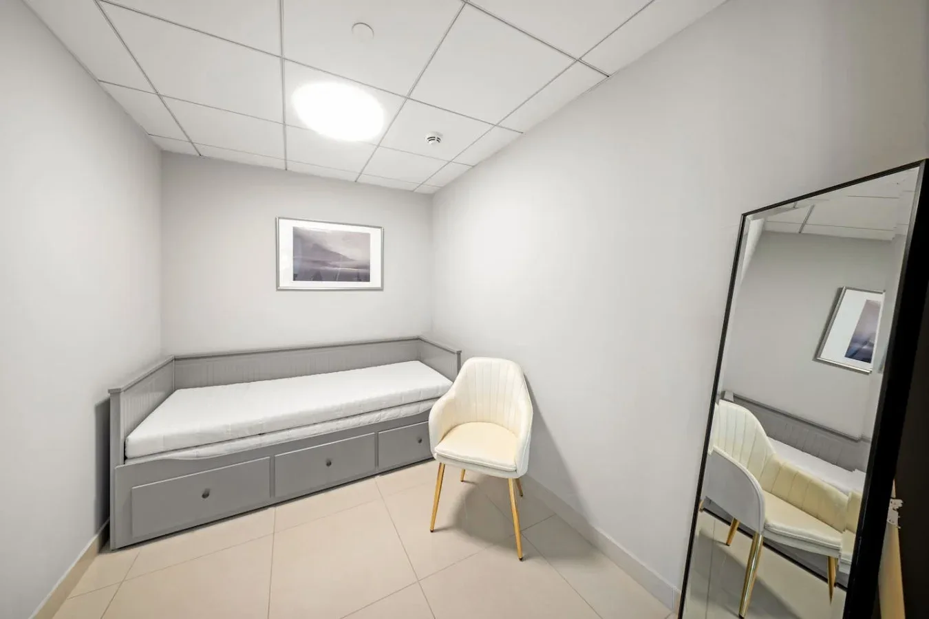 Un cuarto compacto con una cama empotrada, una silla y un espejo de cuerpo entero.