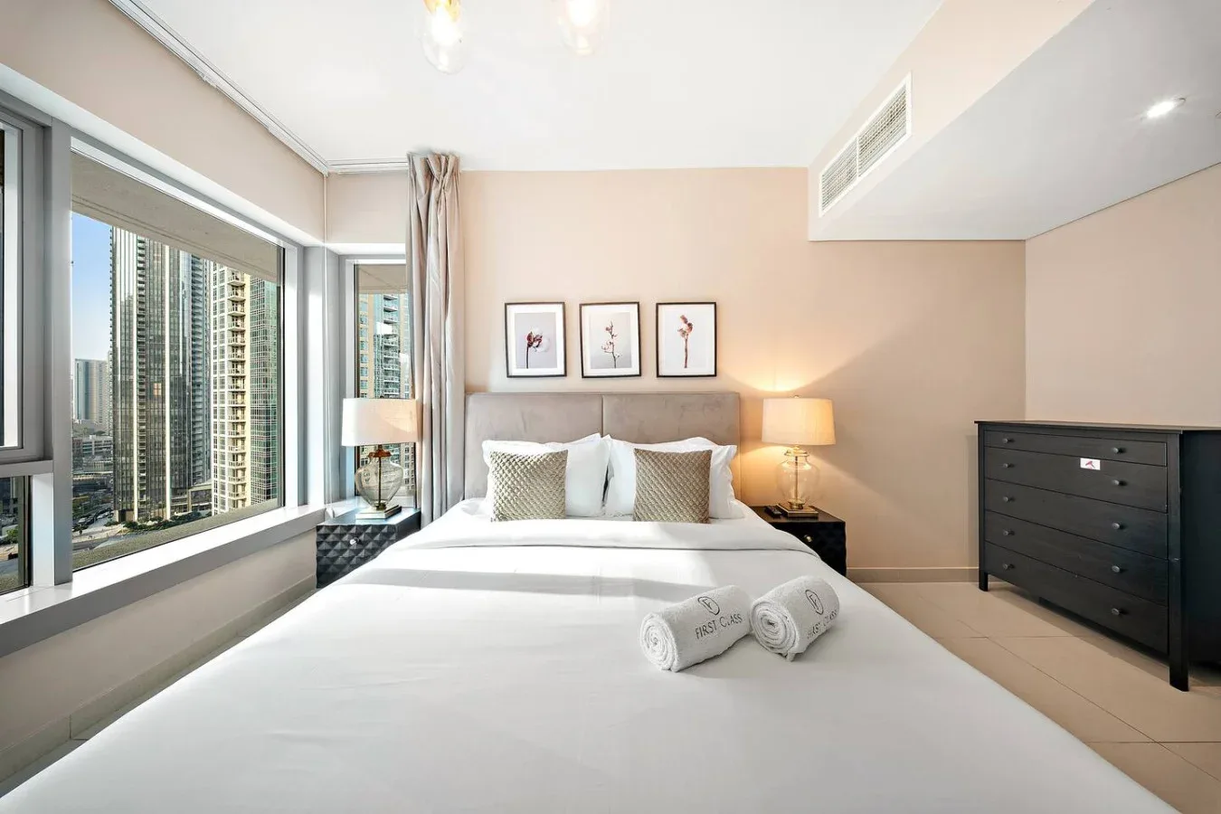 Un dormitorio luminoso con una cama bien tendida junto a grandes ventanas.
