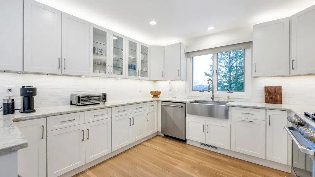 A bright kitchen with white cabinetry, stainless steel appliances, and a window.