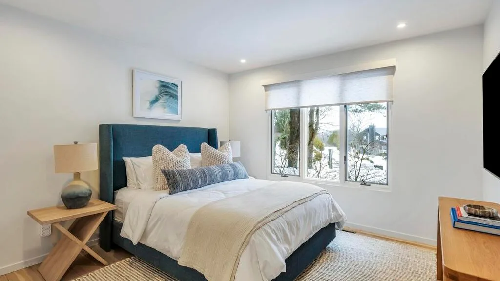 A bright bedroom with a neatly made bed beside a large window.