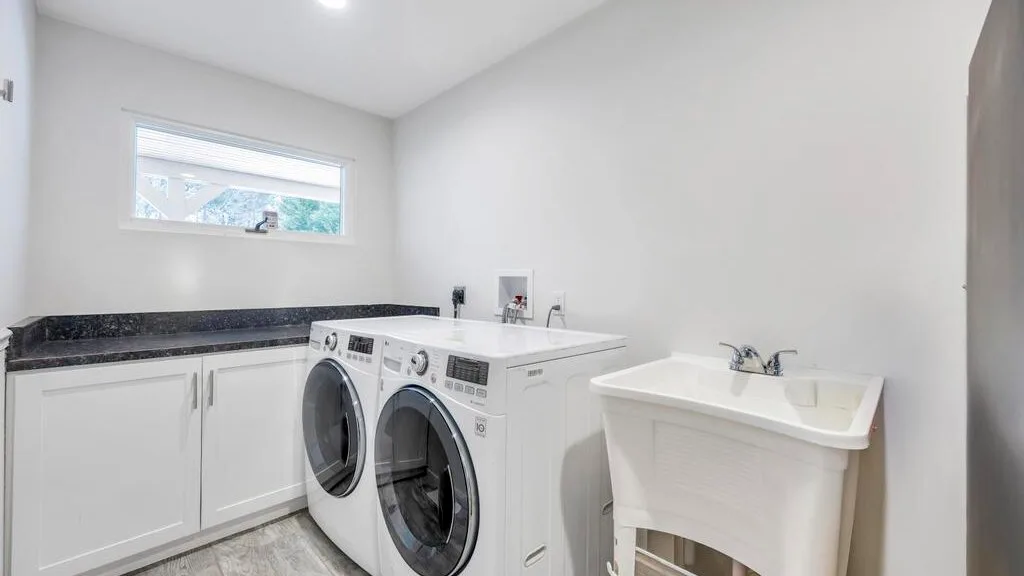 A bright laundry room with front-loading machines and a deep utility sink.