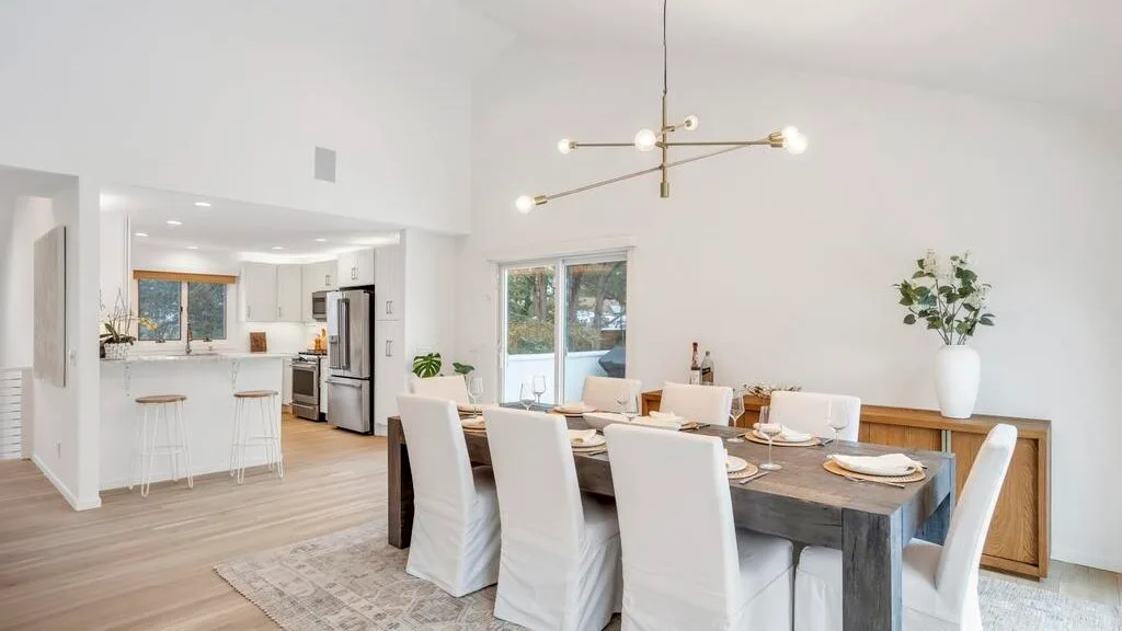 A bright open-plan dining area with a long table beside a kitchen island.