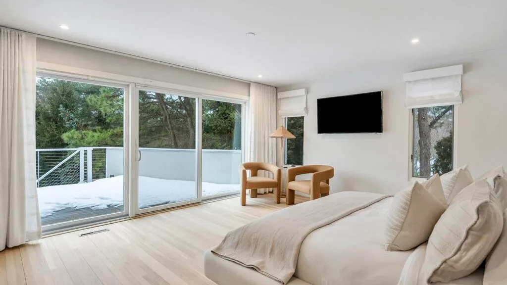 A bright bedroom with a large bed, lounge seating, and sliding glass doors.