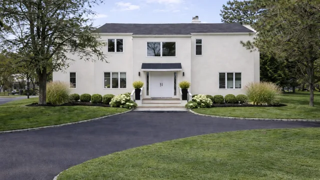A large white house stands beyond a curved driveway, surrounded by trees and lawn.