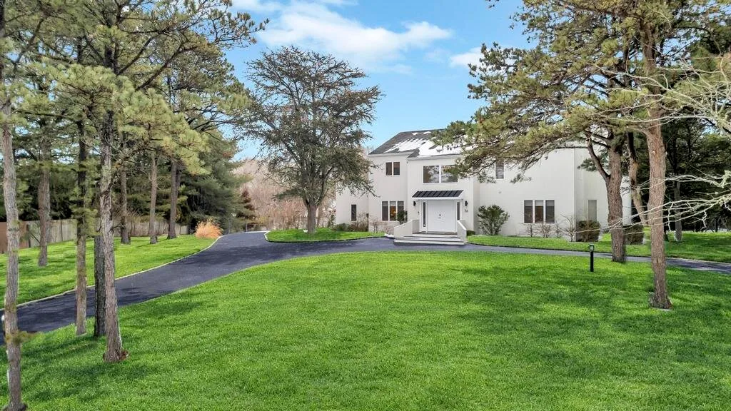 A white house stands beyond a broad green lawn, framed by trees.