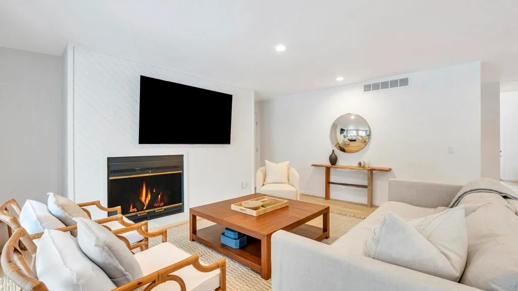 A bright living room with seating around a wooden coffee table and fireplace.