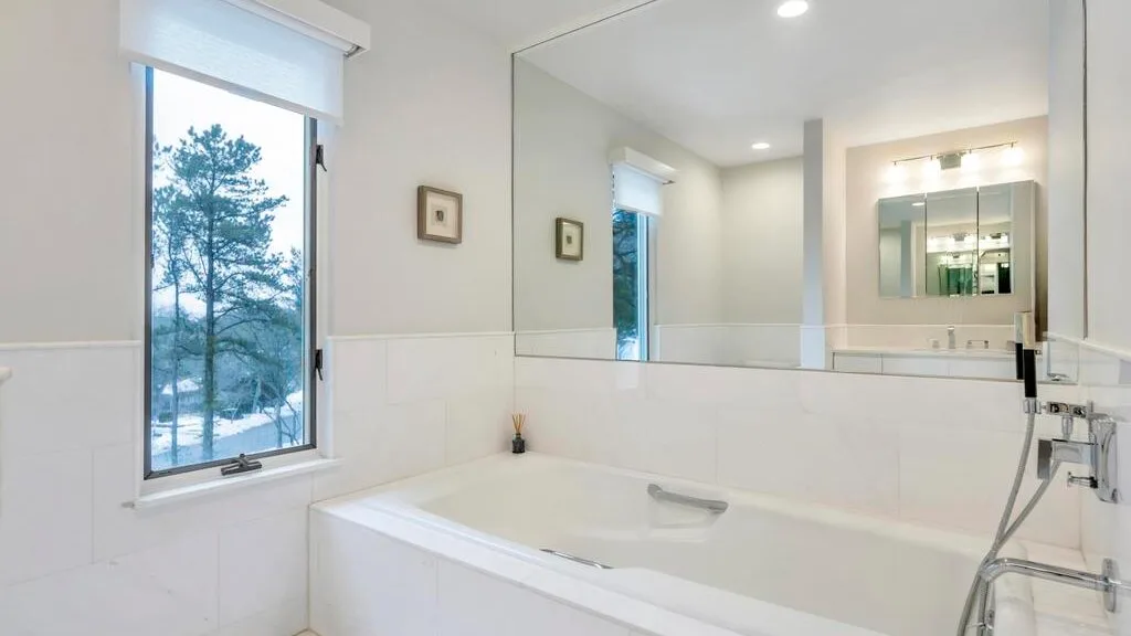 A bright bathroom with a bathtub beneath a large wall mirror.